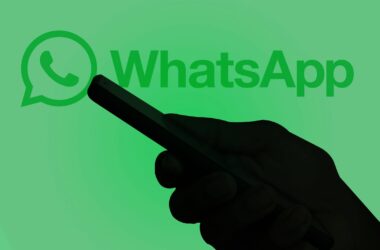Silhueta de pessoa usando celular com logotipo do WhatsApp ao fundo